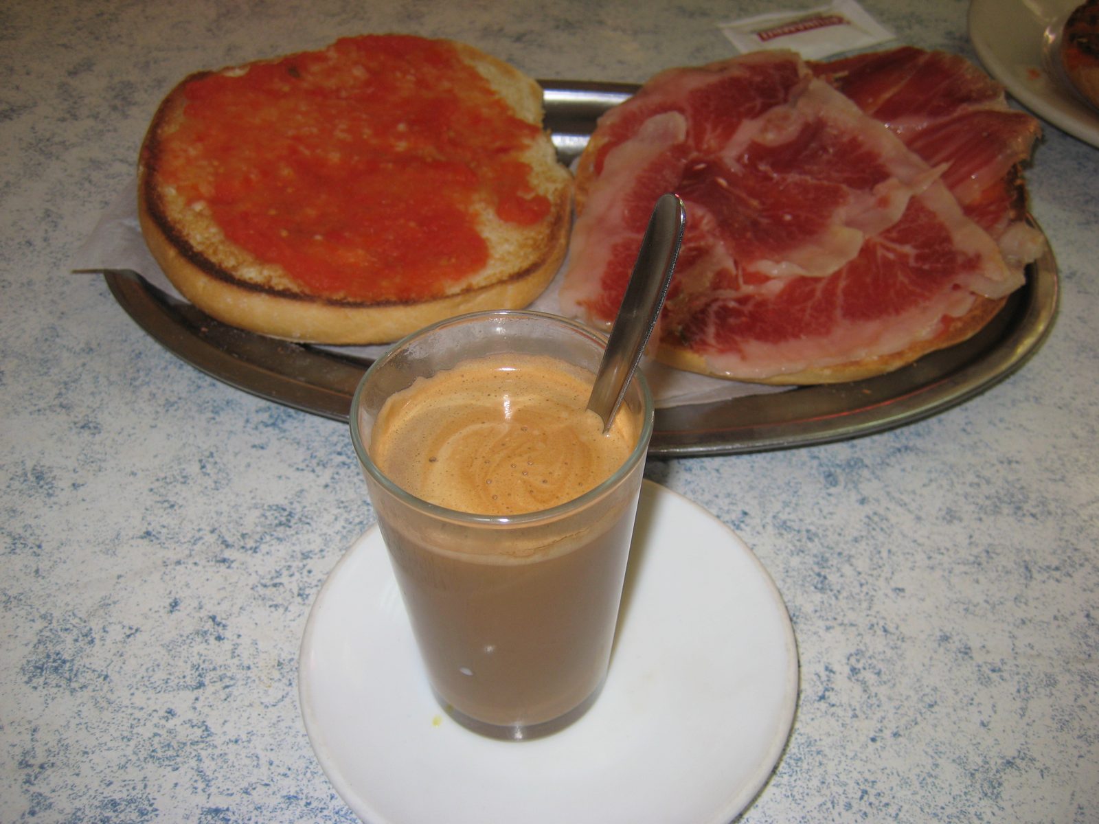 Tostada con tomate, jamón y café con leche en vaso