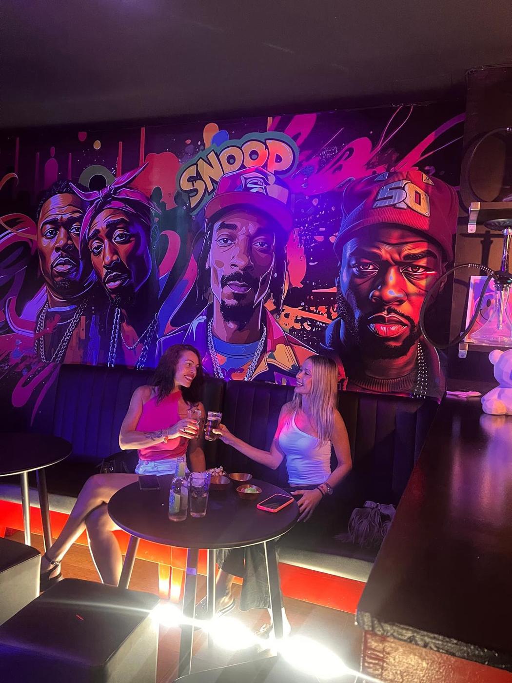 Dos clientas brindando delante del mural de Mi negra